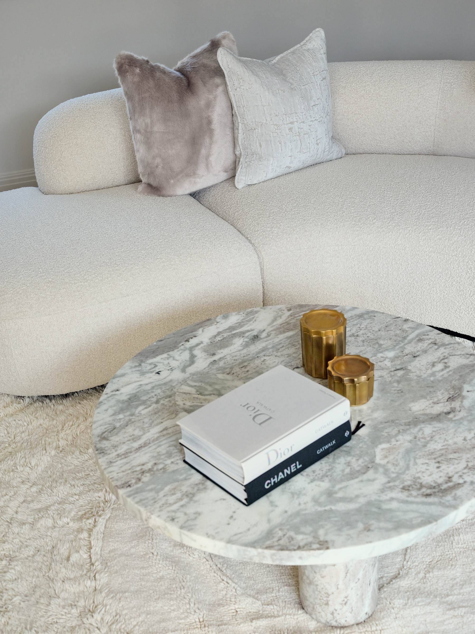Cream boucle curved sofa with round marblel coffee table and textured round rug in living area adjoining kitchen