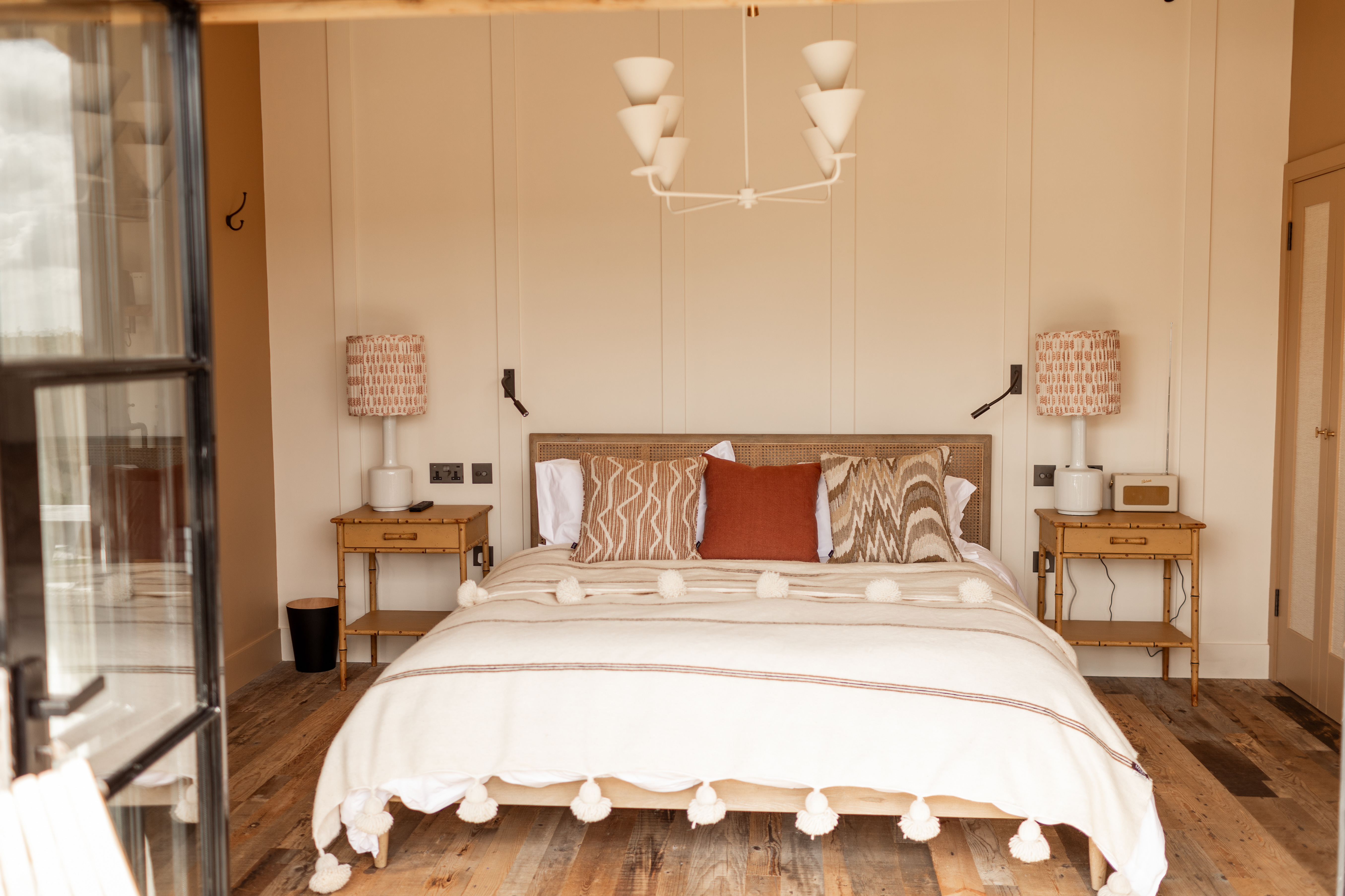 Panelled bedroom with plaster light fitting and natural materials.  Ianthe Porta Romana table lamps and Chelsea Textiles bedside tables.
