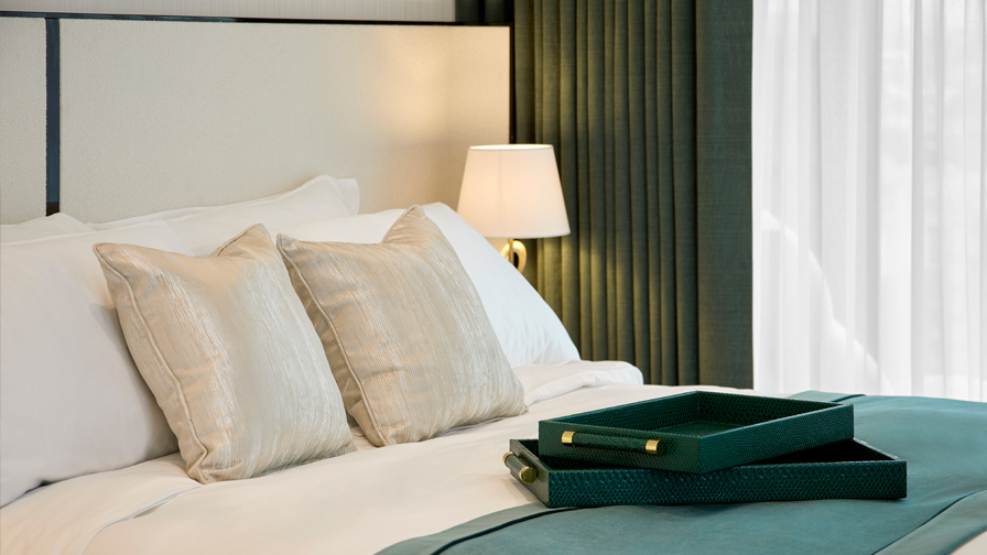 Luxury dining room with white upholstered chairs, pale wood table, modern chandelier, white orchids, and a dramatic backlit onyx feature wall paired with sheer curtains and dark green drapery