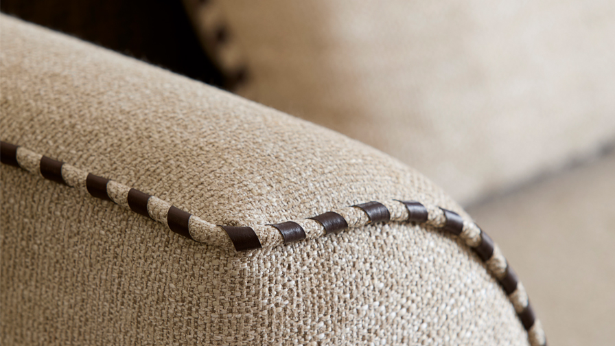 Close-up of luxury sofa arm showcasing high-end upholstery with hand-finished contrast piping in premium textured fabric and leather detailing