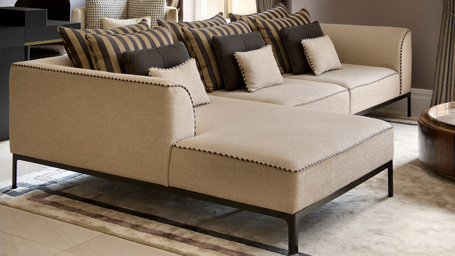 Luxury sectional sofa in neutral fabric with artisan contrast piping, paired with striped and textured accent cushions in a bespoke high-end living room interior