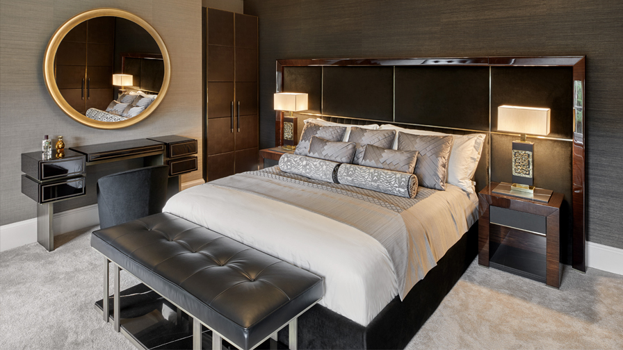 Elegant luxury bedroom with upholstered king bed, custom oversized headboard, designer bedside tables, tufted leather bench, and modern vanity with gold-accented circular mirror