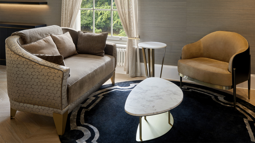 Luxury seating area with designer velvet loveseat, curved armchair, marble-topped coffee table, and dark patterned rug in an elegant contemporary interior