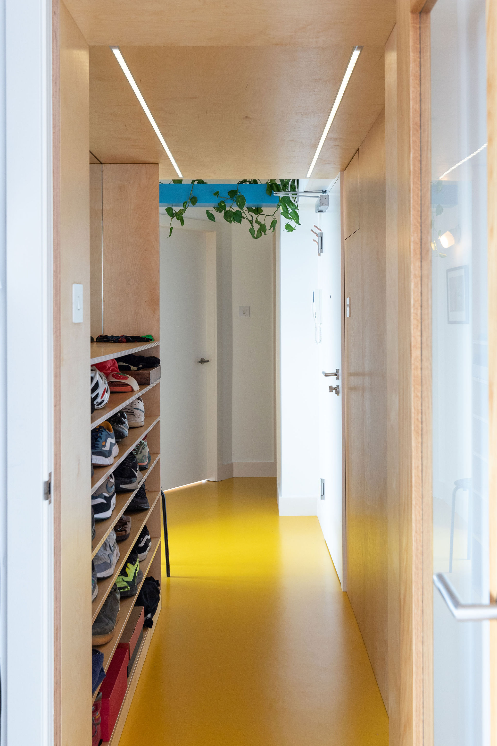 plywood shoe storage, white walls and yellow rubber flooring in the hallway