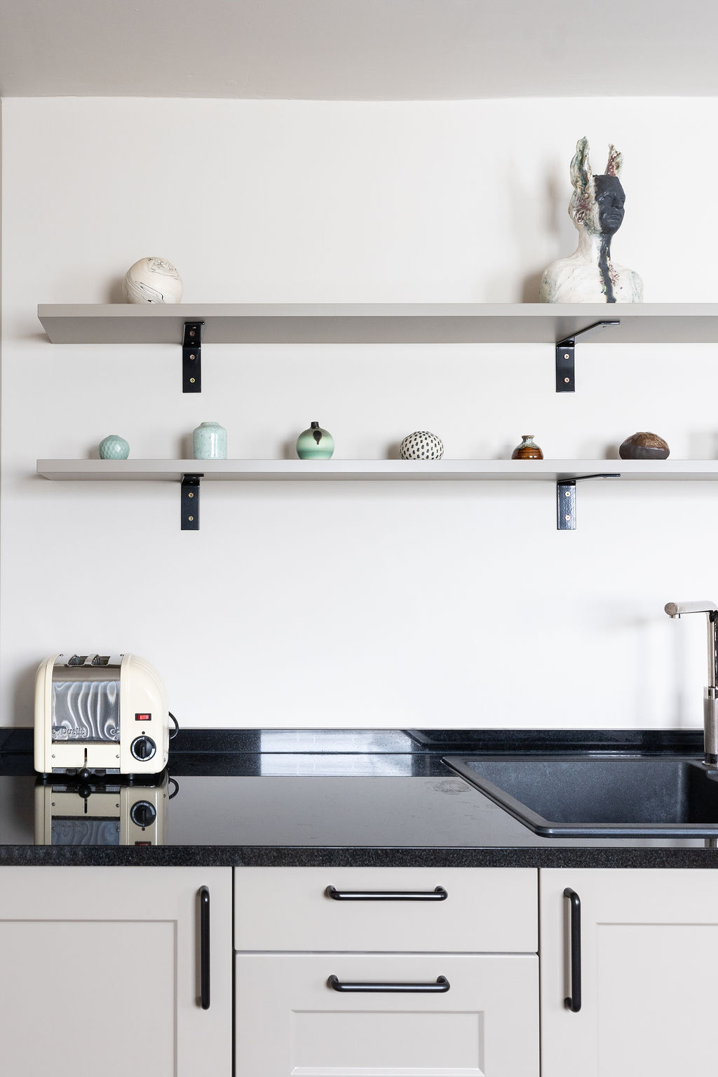 Bespoke neutral kitchen cabinets match the walls and shelving above. Black worktop