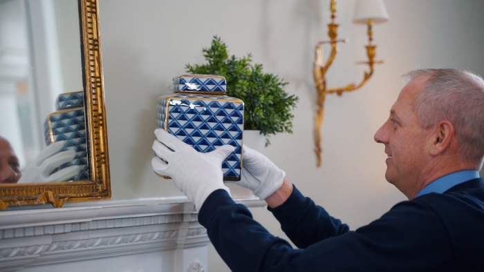man picking up a square blue and white pottery jar.