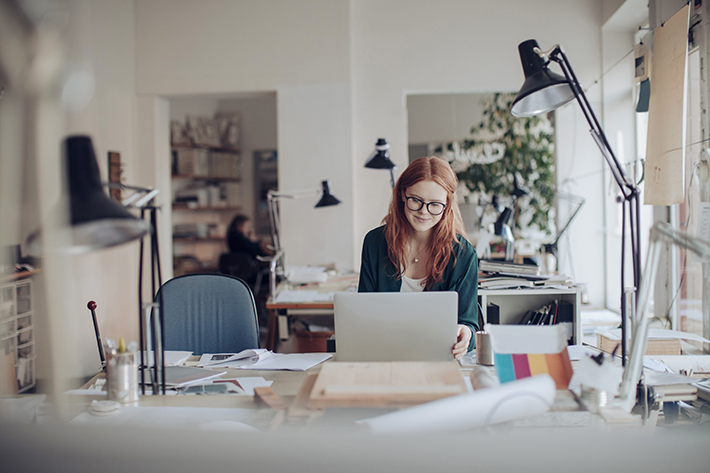 A woman sits at her laptop in her studio