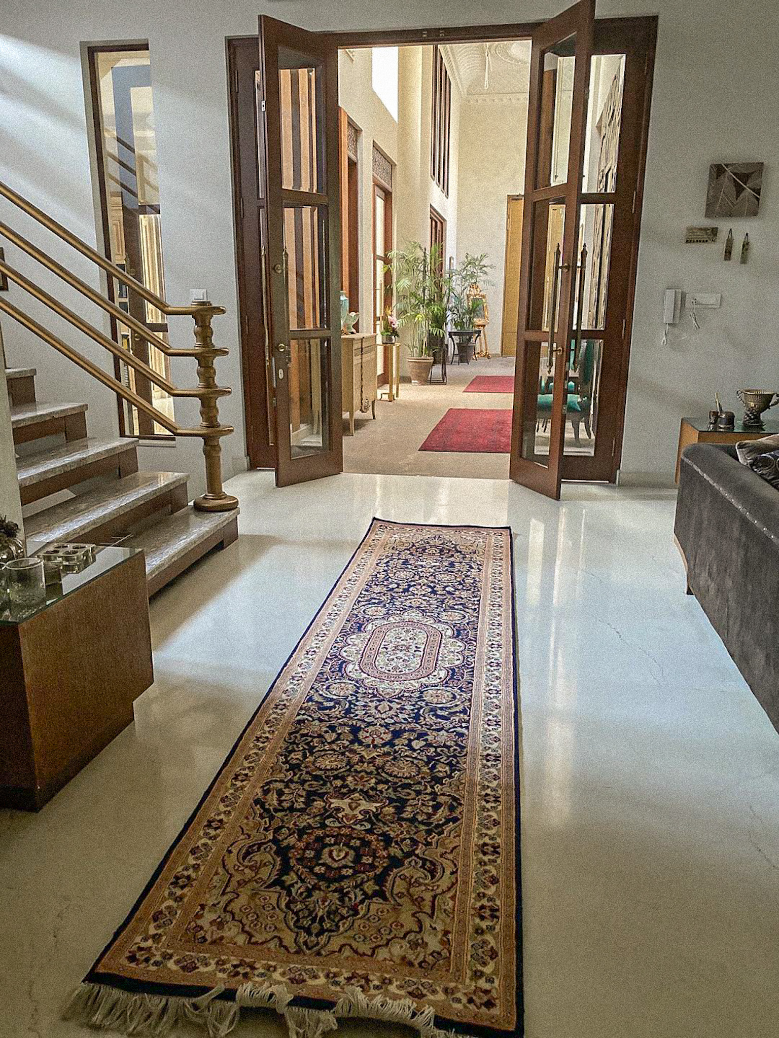 A long, traditional, hand-knotted Pak Persian runner rug in navy blue, red, and cream with a floral pattern, placed on a white marble floor in a spacious, modern hallway.