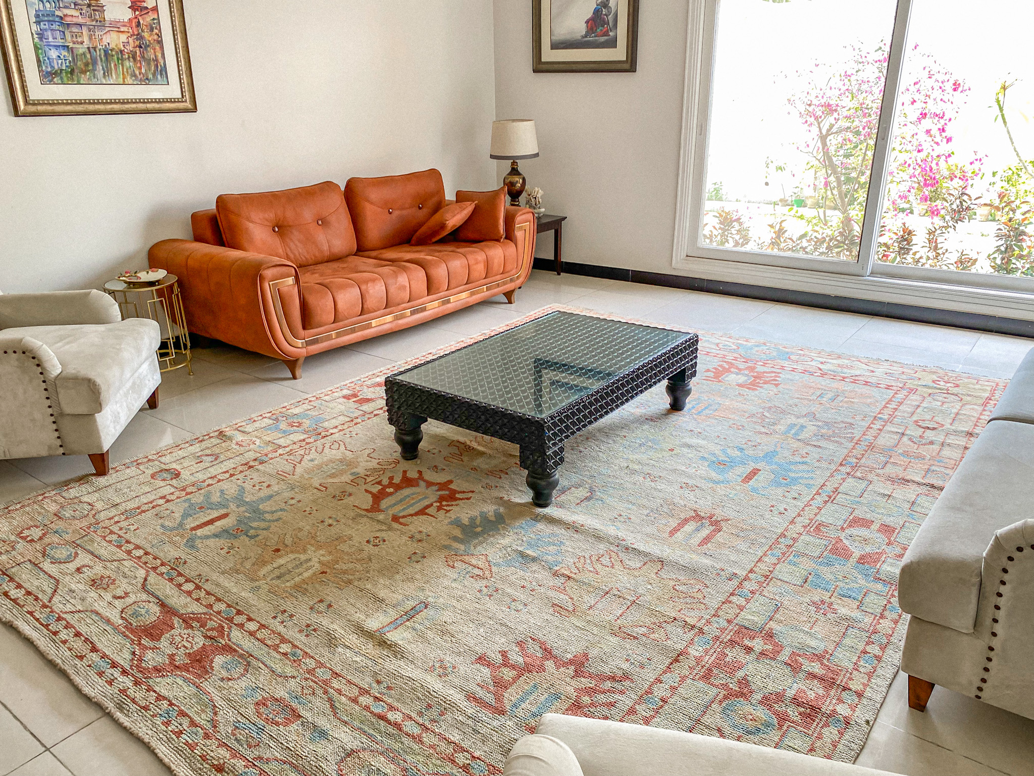 A large, hand-knotted Oushak rug in a modern living room, featuring a traditional, large-scale pattern in faded, muted tones of light blue and rust on a cream field.