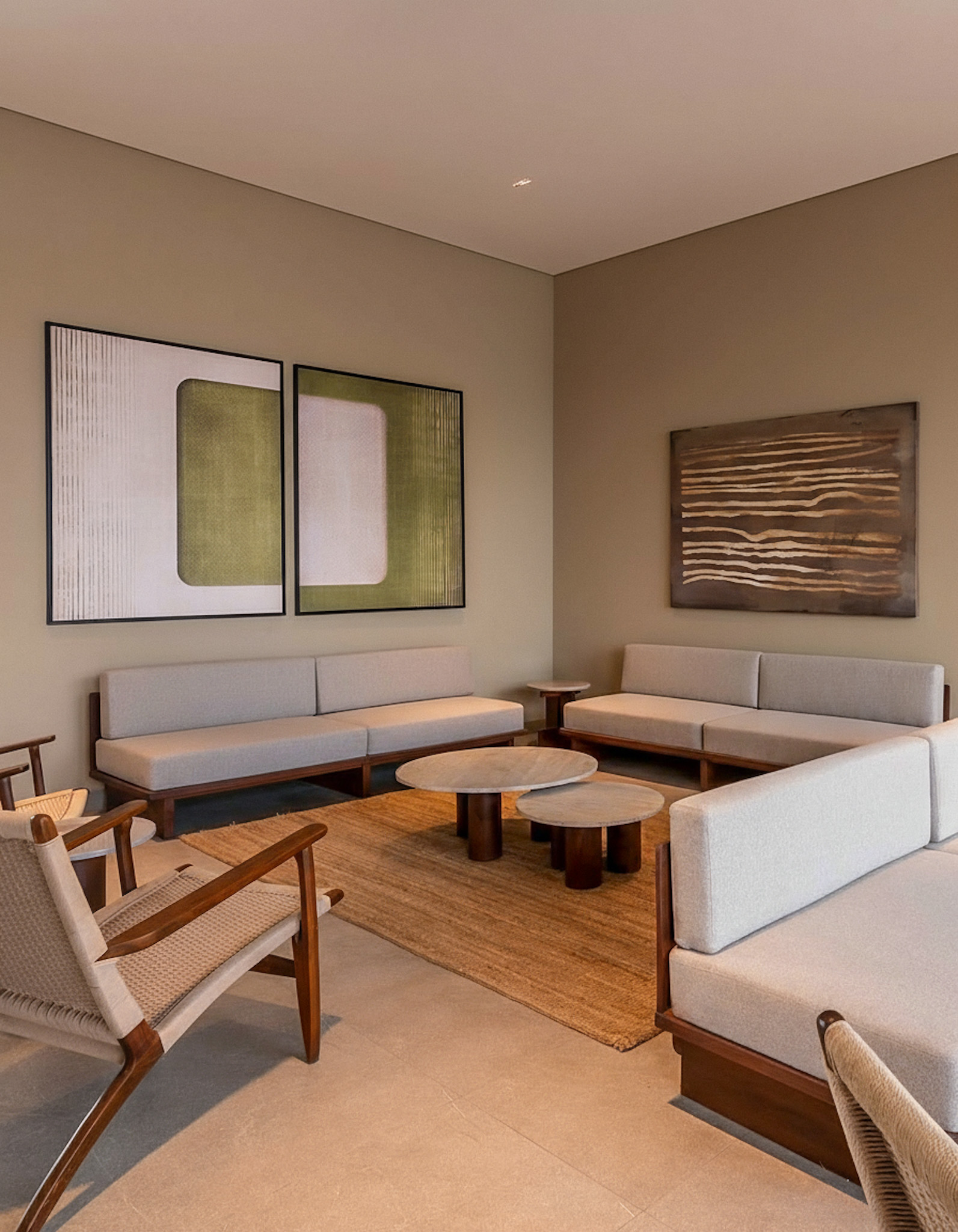 A contemporary resort lounge with minimalist grey sofas and wooden chairs set on a large, plain, natural-fibre jute rug, anchoring the seating area.