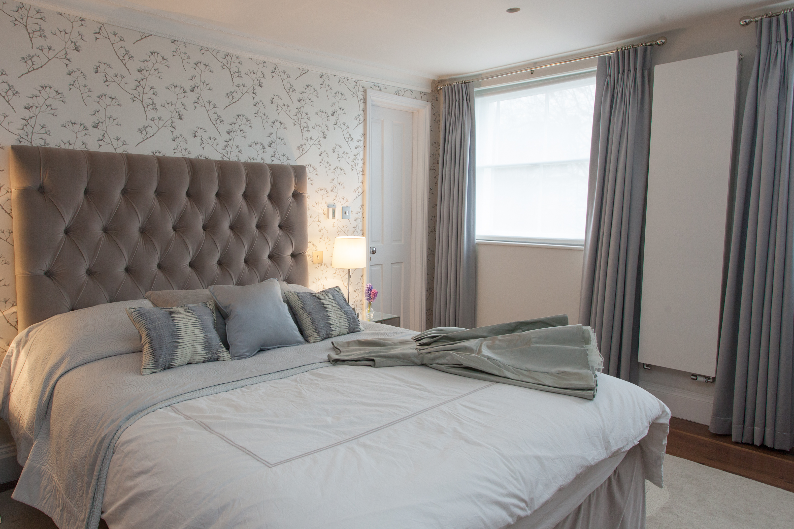 elegant master bedroom in muted colour palette with bespoke headboard and patterned wallpaper