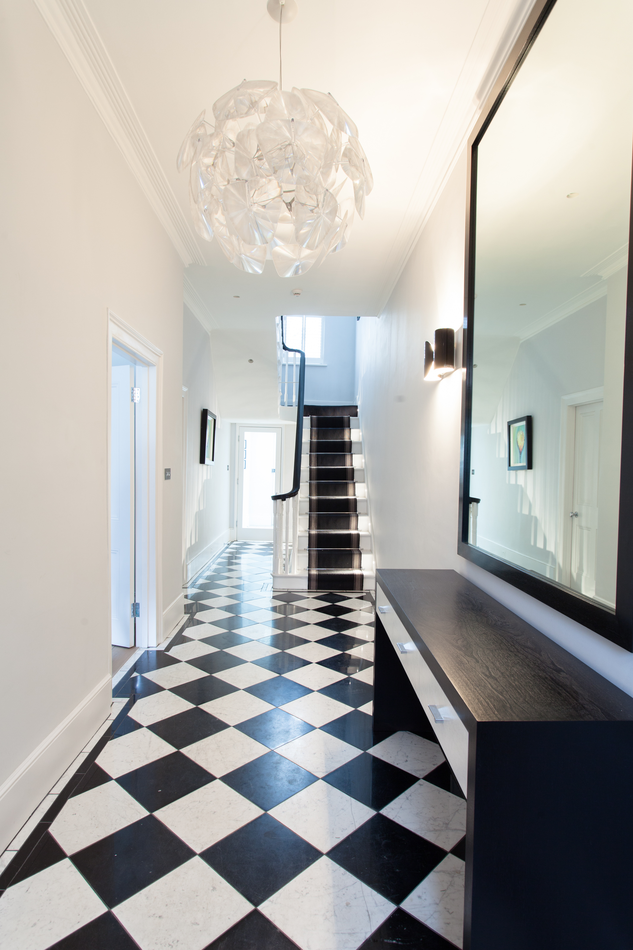 minimalist entrance with black and white floor tiles, dark timber console table and pendant chandelier