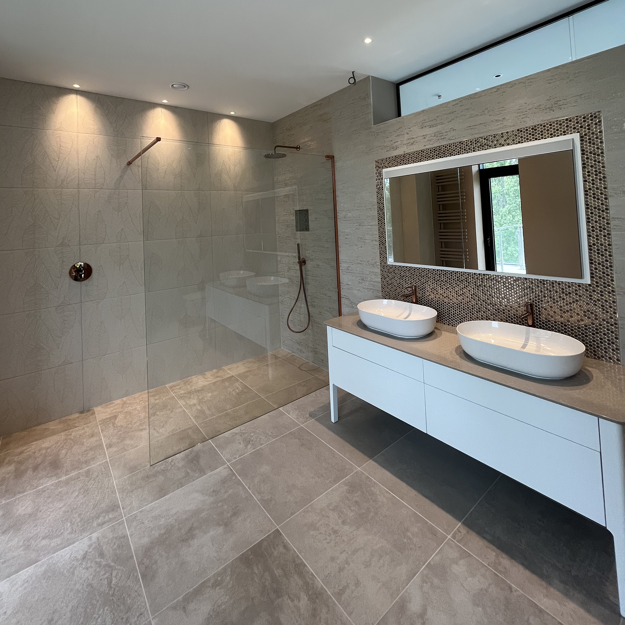 Dual sinks sit on a vanity unit, below a mirror. Also pictured is the floor-level shower