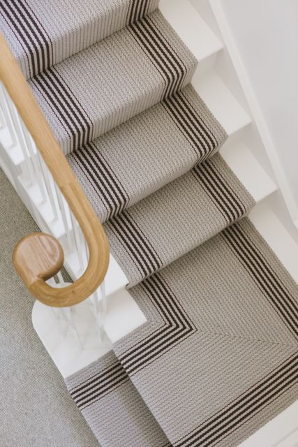 Detail of bespoke staircase with striped Roger Oates stair runner, mitred turn, painted balustrade and round oak handrail in a Cornish cottage.