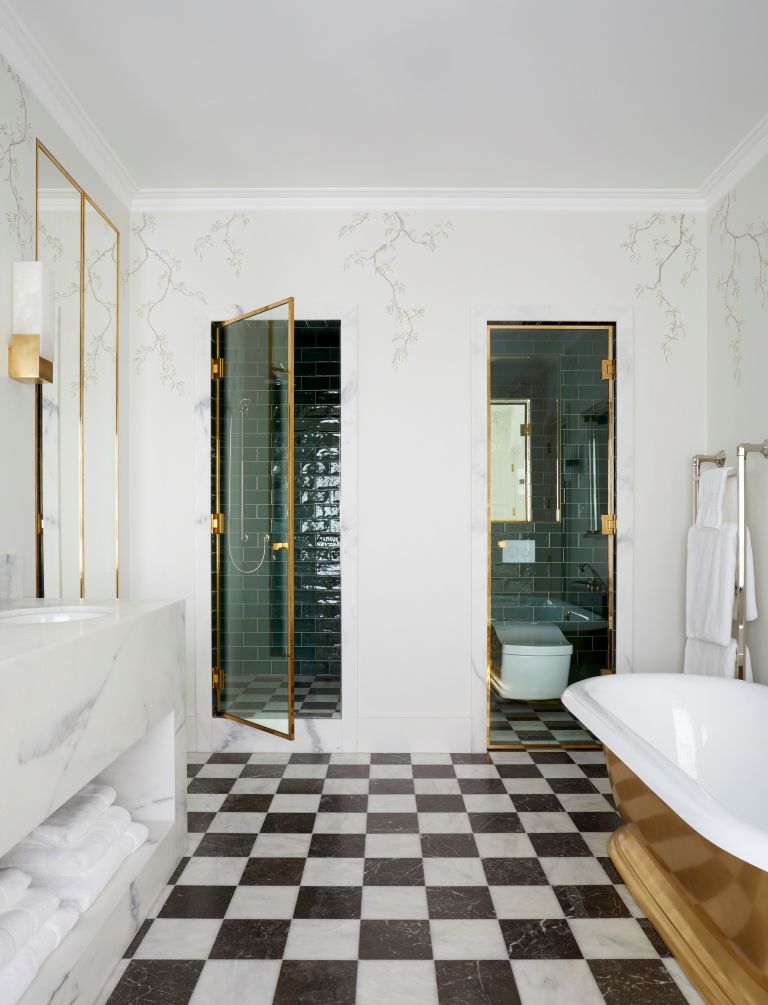 A bathroom with black and white square tiles on the floor, a golden bath and separate toilet and shower cubicles.