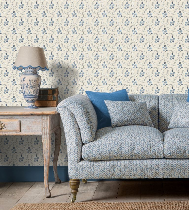 Blue sofa with table and lamp the left and blue and cream patterned wallpaper behind